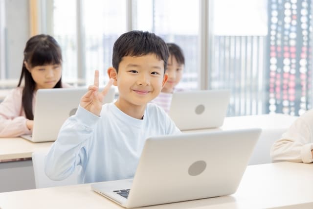 パソコンの前でピースする子ども